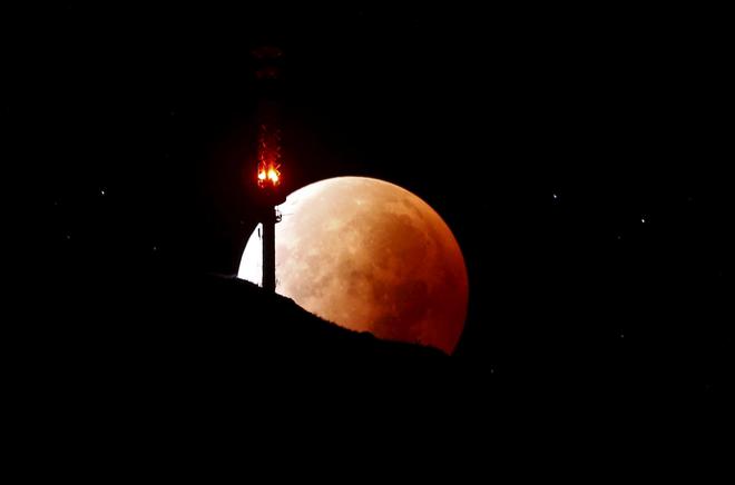 The moon, appearing in a dim red colour, is covered by the Earth's shadow during a total lunar eclipse over the peak of mount Rigi